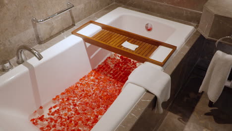 bañera de lujo llena de pétalos rojos, con una bandeja de madera y una toalla en un elegante baño moderno