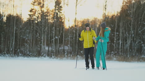 Active-senior-couple-on-skis-moving-down-snowdrift-in-snowfall-during-training-in-winter-forest