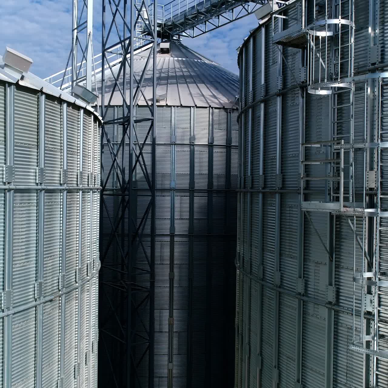 Large metal silo for storing grain. Modern industrial plant. Granary. Silver containers storing agriculture crop. Grain elevators on nature background. Close-up. Motion up.