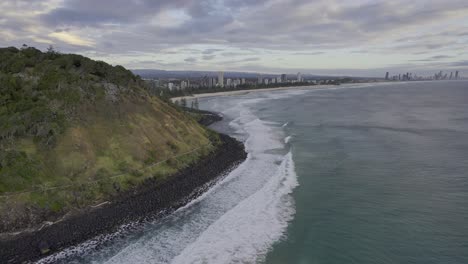 rolling waves onto burleigh heads beach on a cloudy day in gold coast, australia - aerial shot