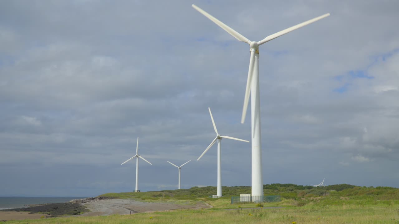 Rotating wind turbines on cloudy summer day with slow parallax pan