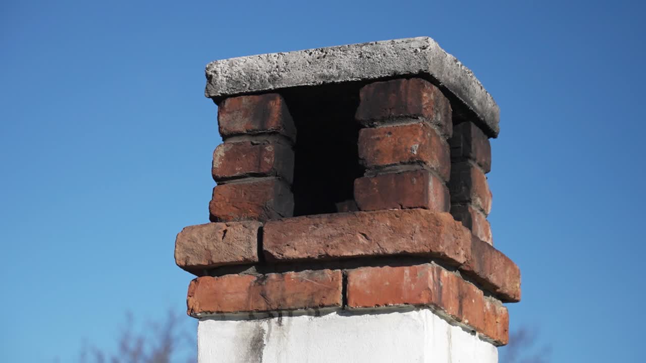 Close-up of a rustic brick chimney against a blue sky