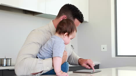 father holding his baby before work and using tablet