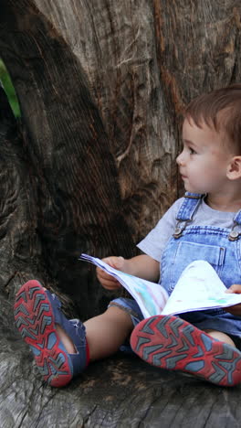 cute lifestyle kid in garden having fun. little boy in park sitting. vertical video