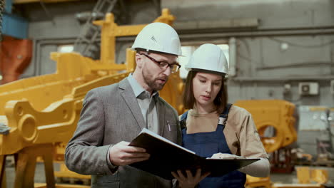 female industrial worker discussing paper plan with male engineer in factory