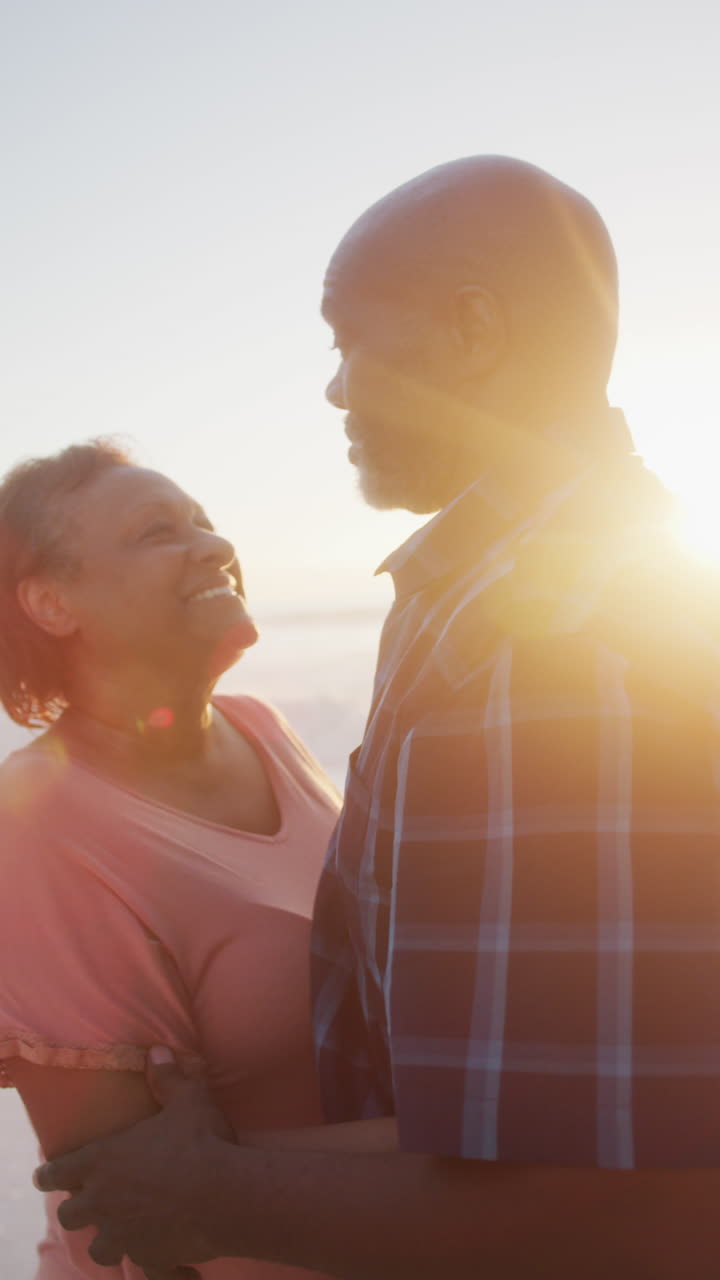 video vertical de una feliz pareja afroamericana de alto nivel abrazándose en una playa soleada