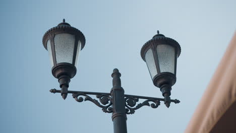 close-up of an ornate black double-lamp post with intricate designs, highlighting textured glass shades against a clear blue sky and partial view of a beige patio canopy