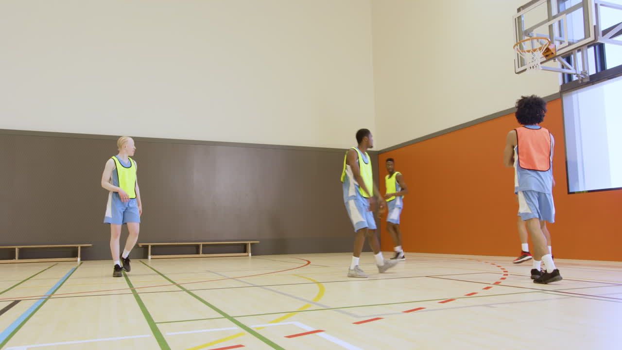 Teen basketball players practicing teamwork and shooting hoops in school gym