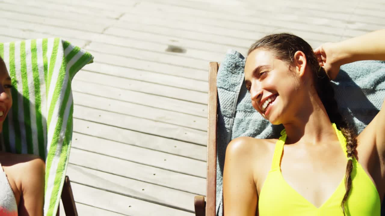 Two womens interacting with each other while sunbathing near swimming pool