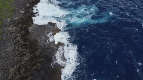 Drone-shot-of-ocean-water-splashing-on-cliff-rocks