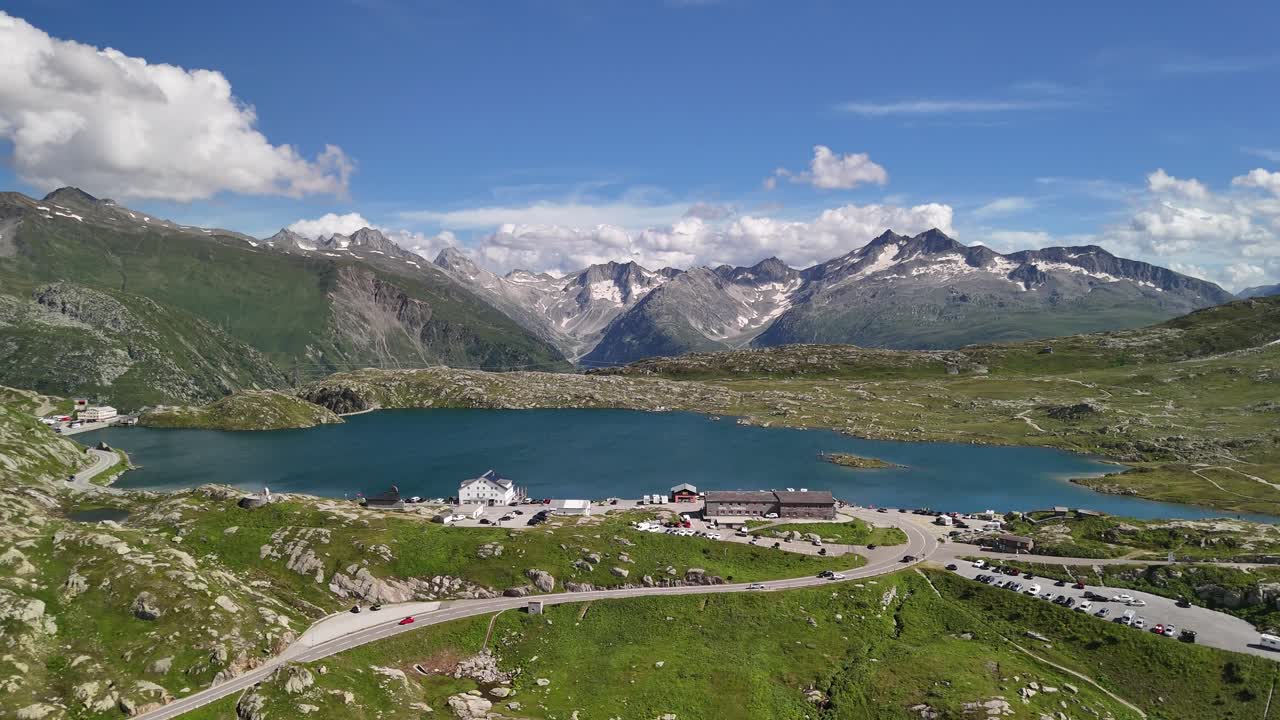 Aerial view of Lake Totensee nestled within the mountain range in Obergoms, Switzerland, showcasing the dramatic contrast between the serene lake and the rugged alpine terrain.