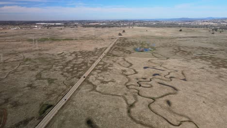 una carretera con autos conduce a través de un campo rodeado de piscinas vernales estacionales protegidas en el valle central de california