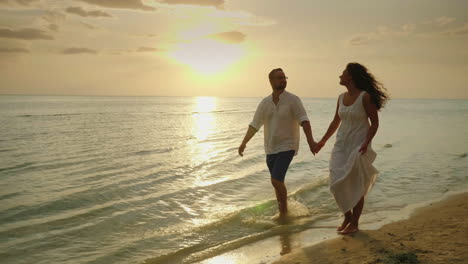 Joven-Pareja-De-Enamorados-En-Ropa-Ligera-Sin-Preocupaciones-Corriendo-En-Una-Playa-Tropical-Limpia