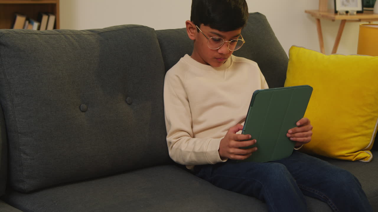Young Boy Sitting On Sofa At Home Playing Games Or Streaming Onto Digital Tablet 2