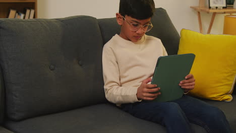 young boy sitting on sofa at home playing games or streaming onto digital tablet 2
