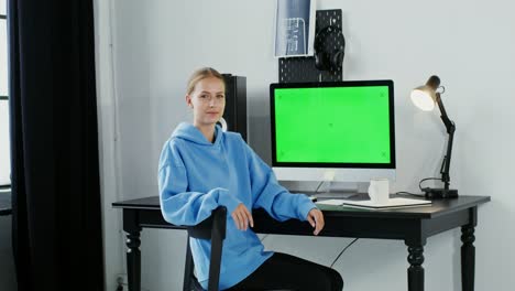 woman working at a home office with a green screen computer