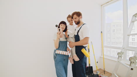 familia mirando un teléfono móvil en la habitación que están pintando