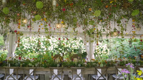 panning sliding shot of exquisite long banquet table decorated in fairytale theme surrounded by flowers