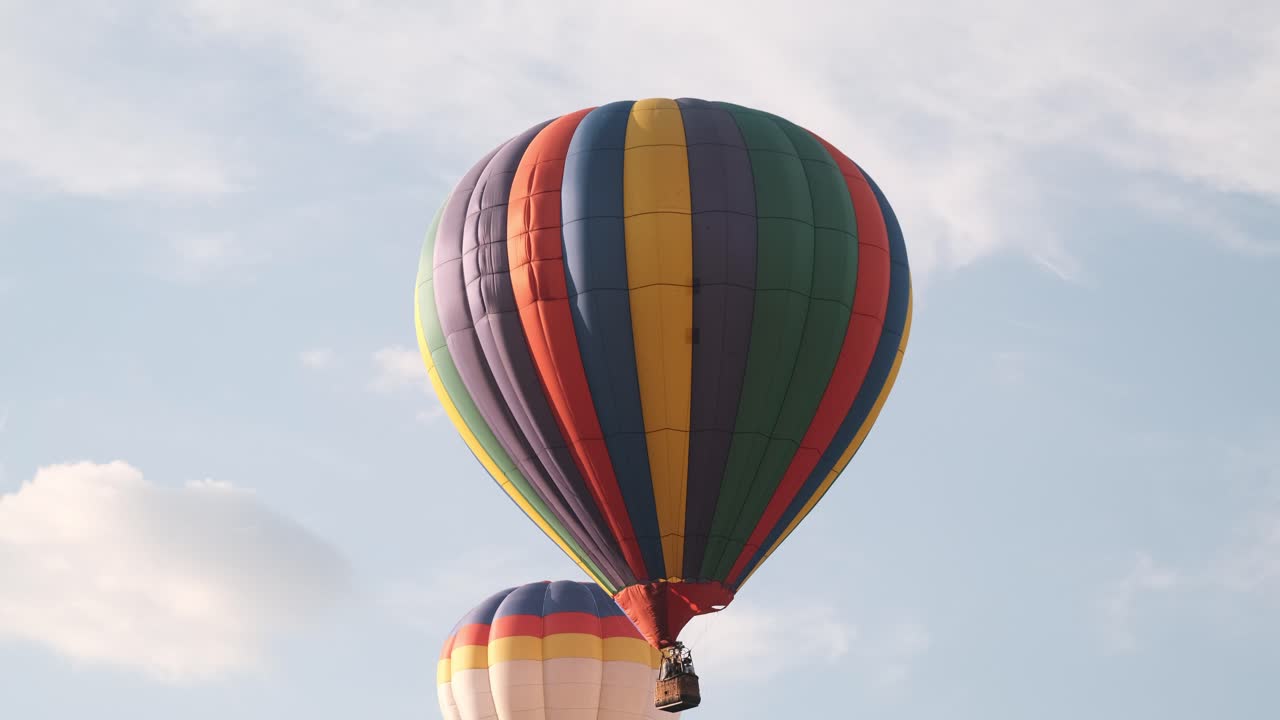 Lenta carrellata di mongolfiere colorate che si muovono oltre nuvole gonfie.