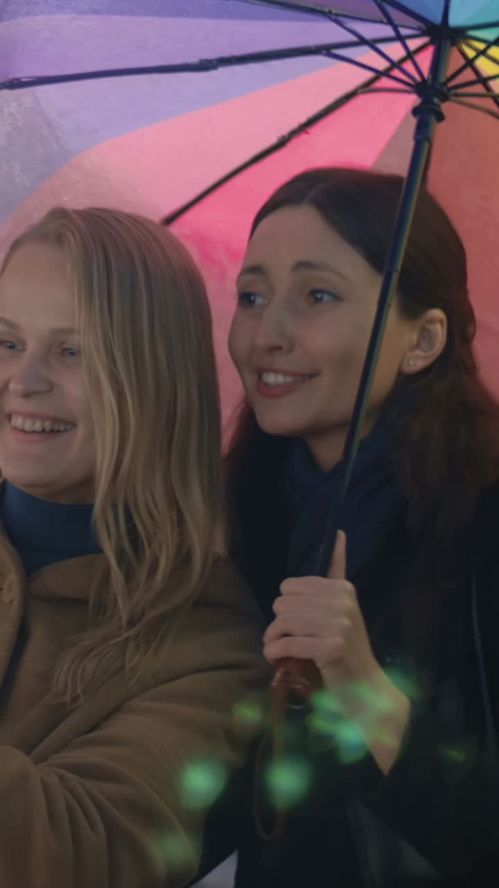 Due donne sotto un ombrello colorato che guardano uno smartphone