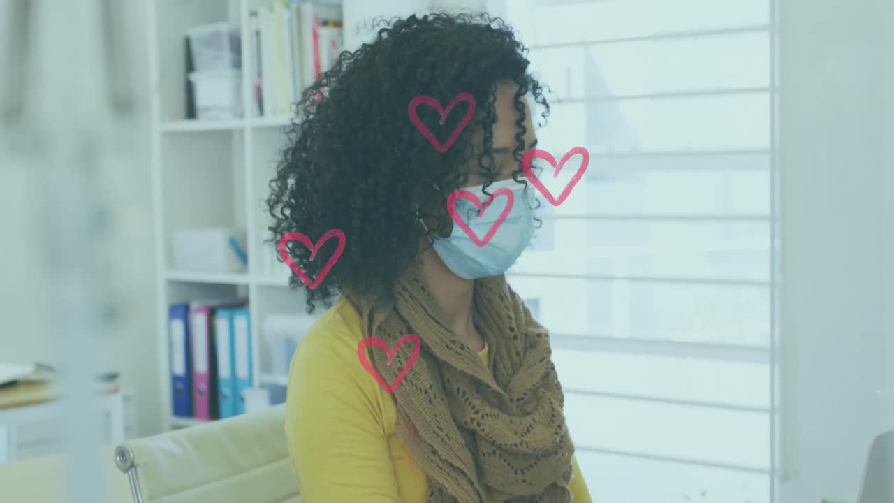 Icone multiple di cuori rossi che fluttuano sopra una donna afroamericana che indossa una mascherina e lavora in ufficio