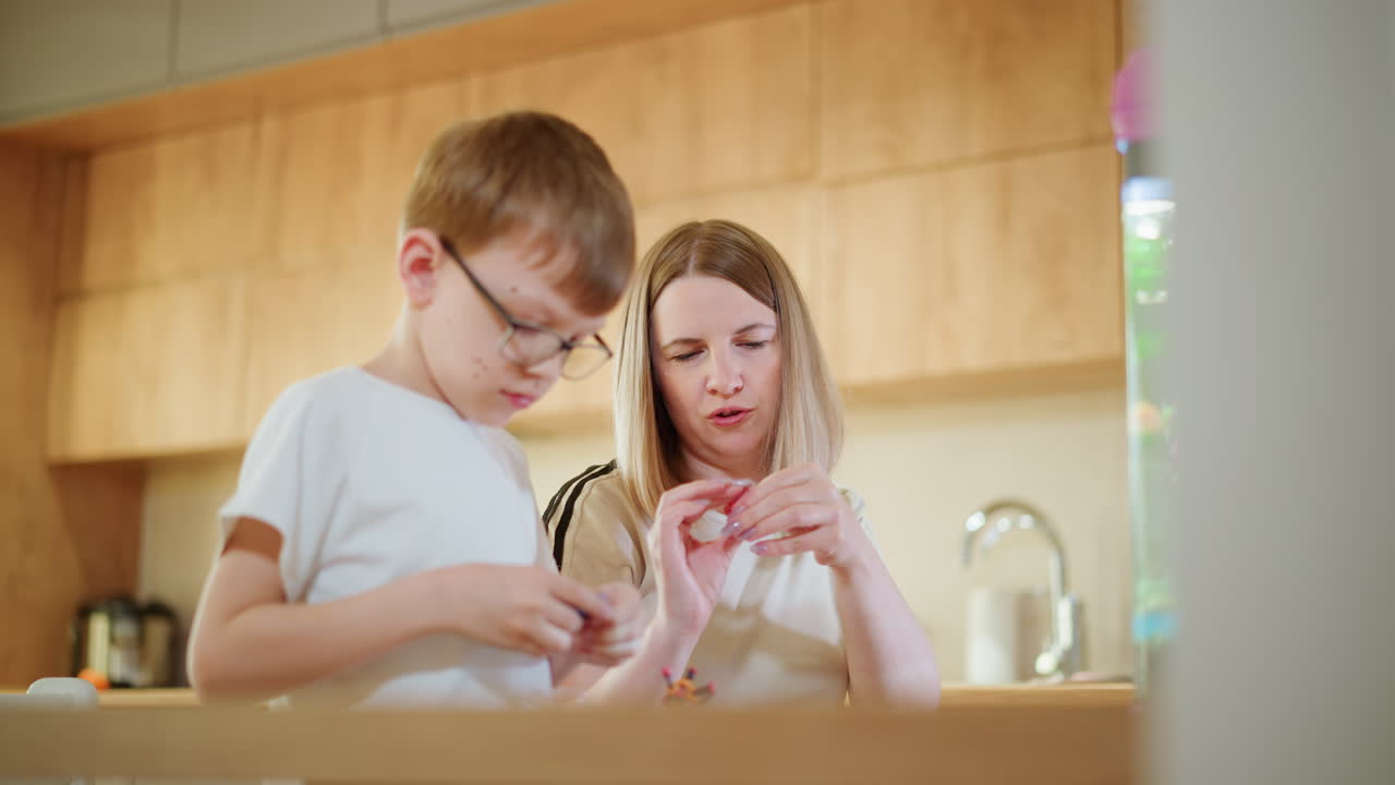 Mother and son sitting at kitchen table near aquarium, focused on creative activity with colorful clay, enjoying fun bonding time while shaping and crafting handmade objects together in bright home