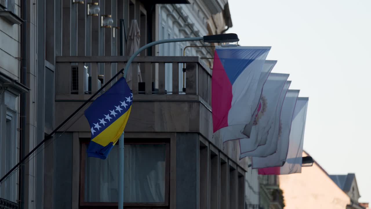 Bosnia and Czech flags flutter on embassy facade in Prague, daylight, static camera, urban setting