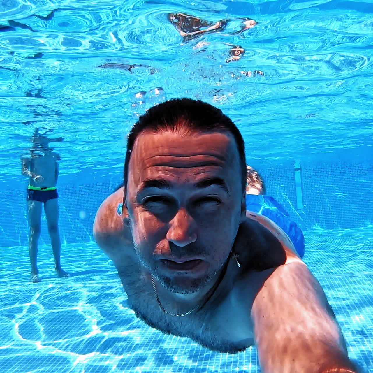 Man swims underwater in the pool. Blue clear water and a male swimming ahead with underwater camera. Summer vacation at water.