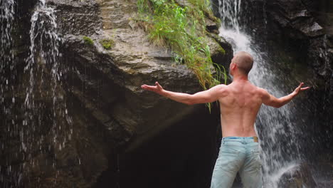 hombre sin camisa feliz de vincularse con la naturaleza cerca de la cascada