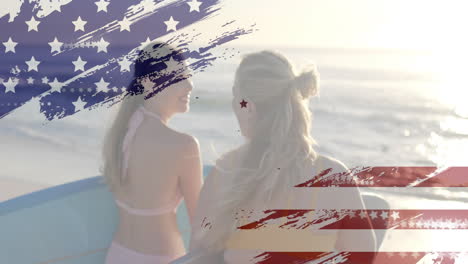 animation of flag of usa over happy caucasian women with surfboards on beach in summer