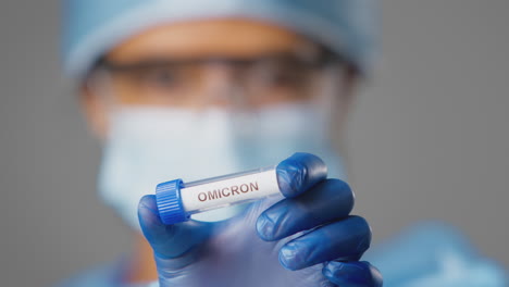 primer plano de una investigadora de laboratorio que lleva un ppe con un tubo de ensayo etiquetado como omicron