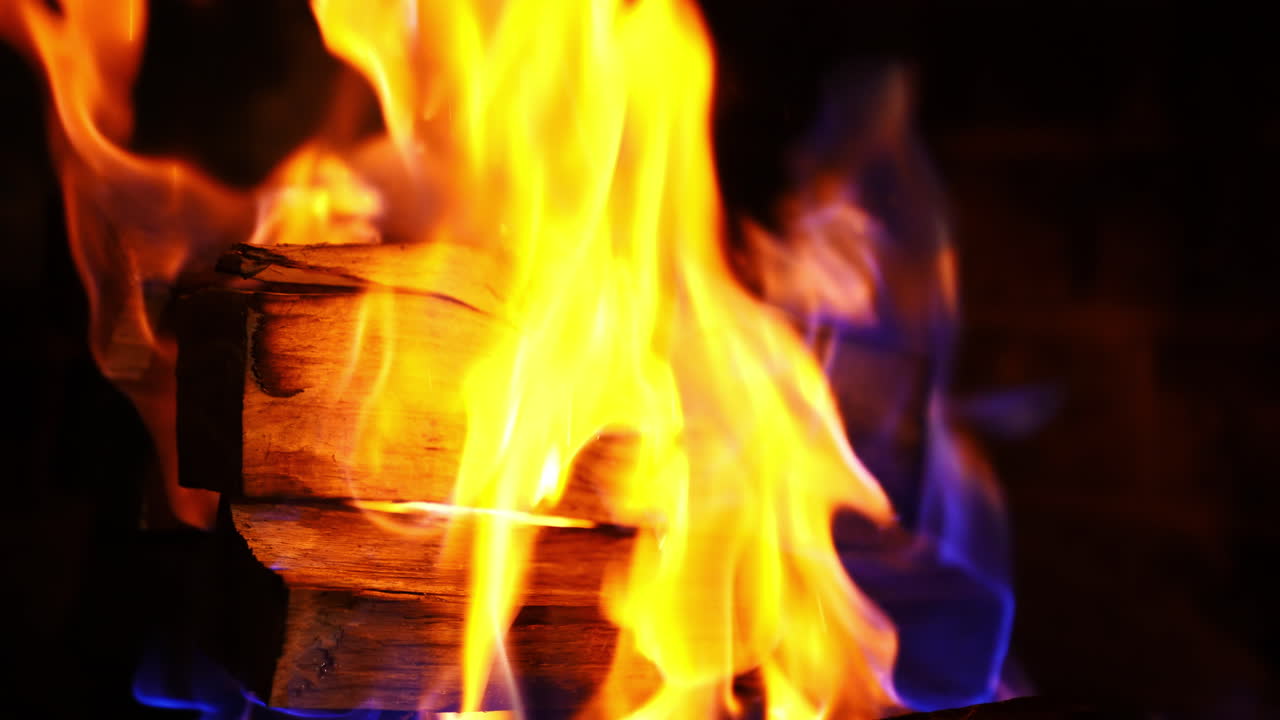 Blue and orange flame over wood. Fire ignited in a fireplace. Vivid flame on black background. Burning wooden logs. Close-up.