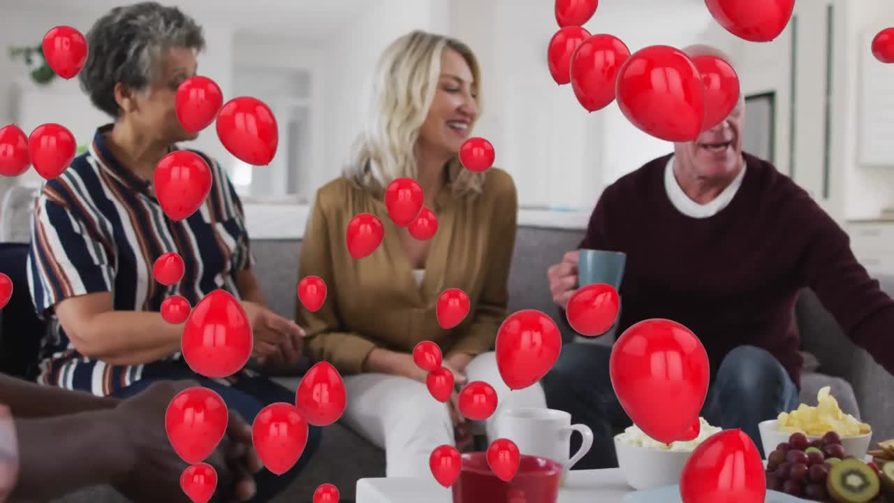 Múltiples globos rojos flotando sobre dos parejas mayores diversas desayunando juntos en casa.