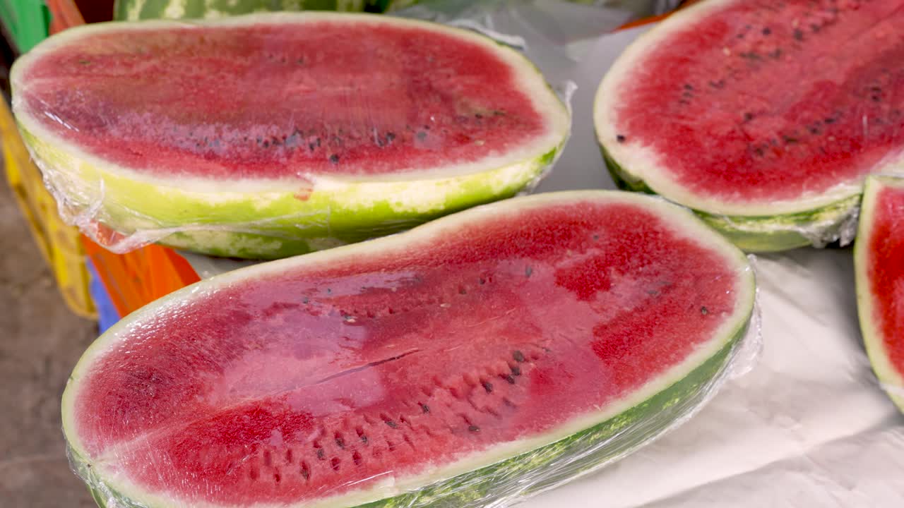 In a lively market, glistening slices of juicy watermelon rest in their clear wraps. Enthusiastic vendors showcase their colorful offerings as shoppers explore the vibrant atmosphere