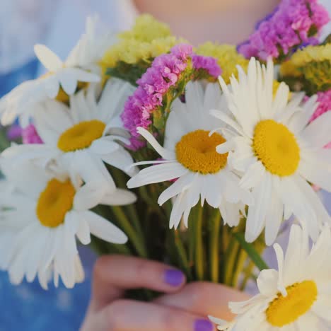 blonde girl holds a bouquet of flowers stands in a meadow at sunset 1