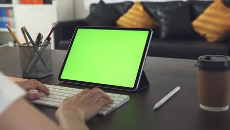 mujer sosteniendo una tableta digital con pantalla verde y trabajando, escriba el teclado en el escritorio de la oficina.