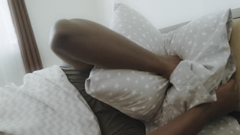 Upset-man-lying-in-bed-in-morning.-African-adult-covering-head-with-pillow.