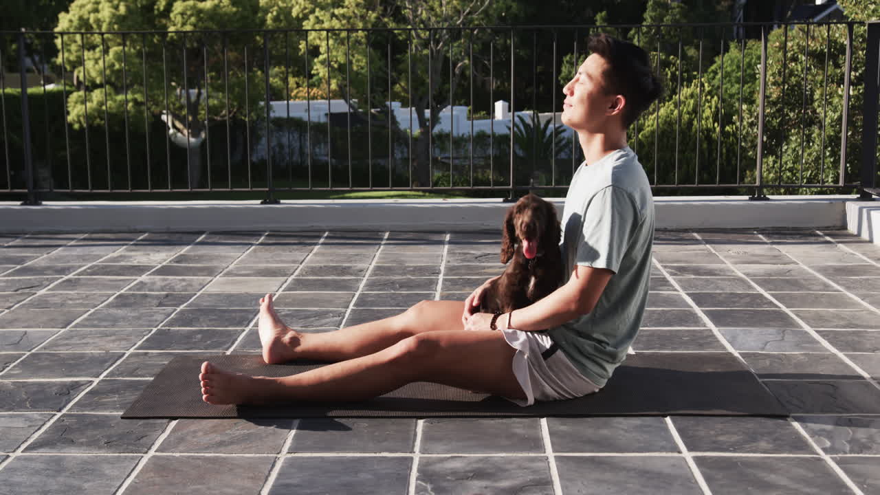 Relaxing outdoors, Asian man sitting with dog on patio enjoying sunlight