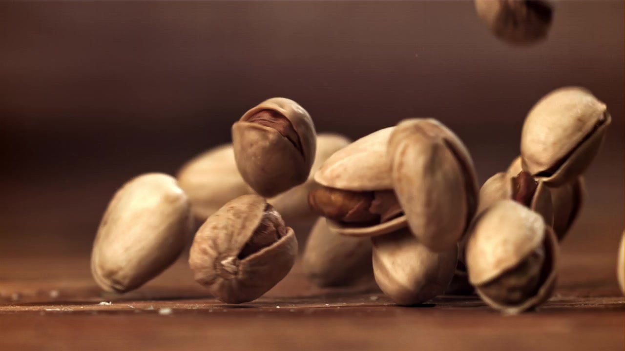 Close-up of Pistachio Nuts Falling onto a Wooden Table