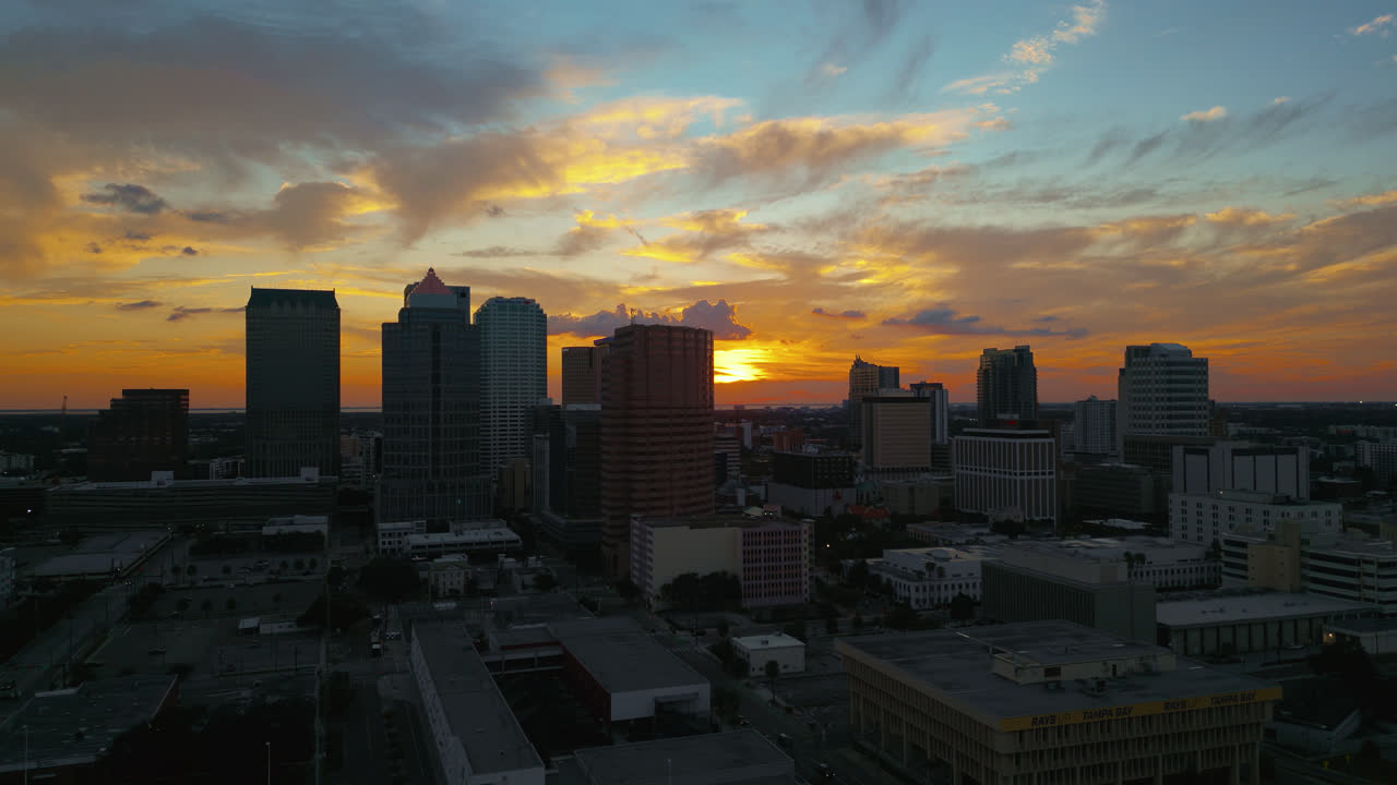 Tampa skyline at sunset with glowing yellow sky and silhouetted buildings, aerial tracking to the right