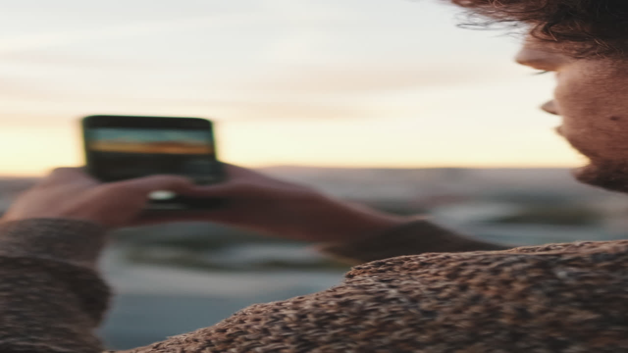 Man taking picture of cityscape at sunset with smartphone