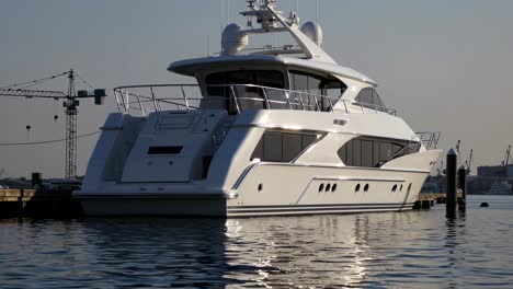 large white luxury yacht moored at the dock in a shipyard, reflecting beautifully on the calm water of the harbor under a bright sunny sky, creating an elegant maritime scene
