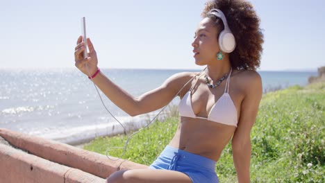 female wearing swimsuit top and blue shorts taking selfie