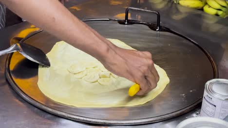 a street vendor skillfully prepares banana roti on a hot griddle in phuket, showcasing traditional thai street food techniques