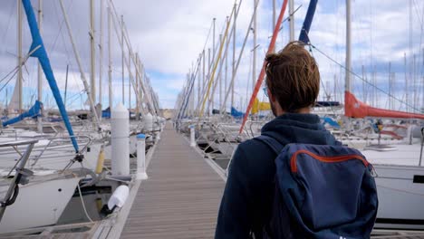 slow motion shot of a man walking along a marina dock towards his yacht