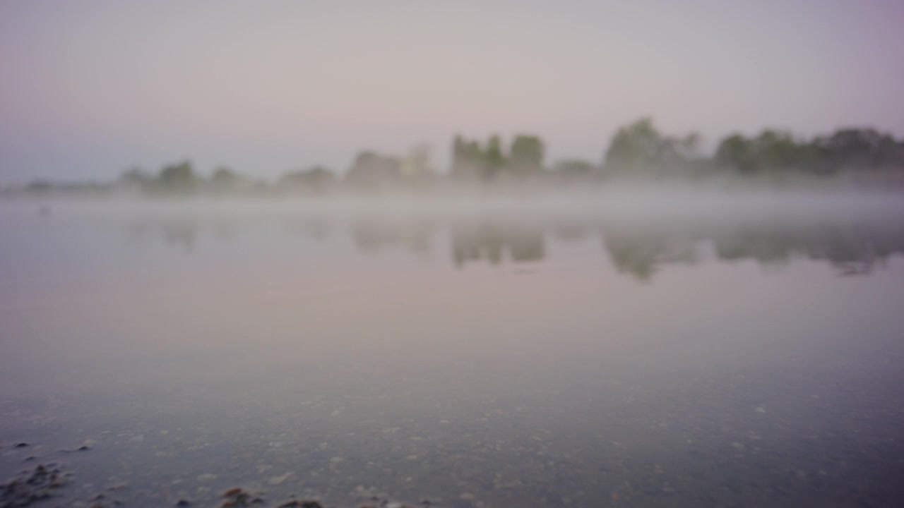 Tranquil mist over a calm lake at dawn with soft reflections on the water, capturing peaceful morning atmosphere and natural serenity in a foggy lakeside landscape