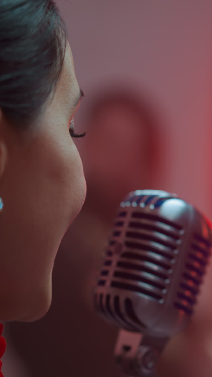 뒷면에서 열정적인 여성 가수가 흐릿한 빨간색 배경으로 빈티지 마이크로 노래하는 클로즈업