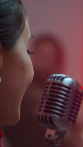 primer plano de una cantante femenina apasionada desde la espalda, cantando en un micrófono vintage con un fondo rojo borroso
