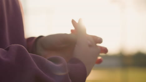 close-up of woman hand in maroon clothing performing wrist twist, sunlight creating a glow effect around hand, with outdoor setting and green background