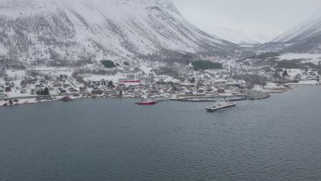 Boat-departs-snow-covered-Olderdalen-ferry-pier,-arctic-winter-aerial-view